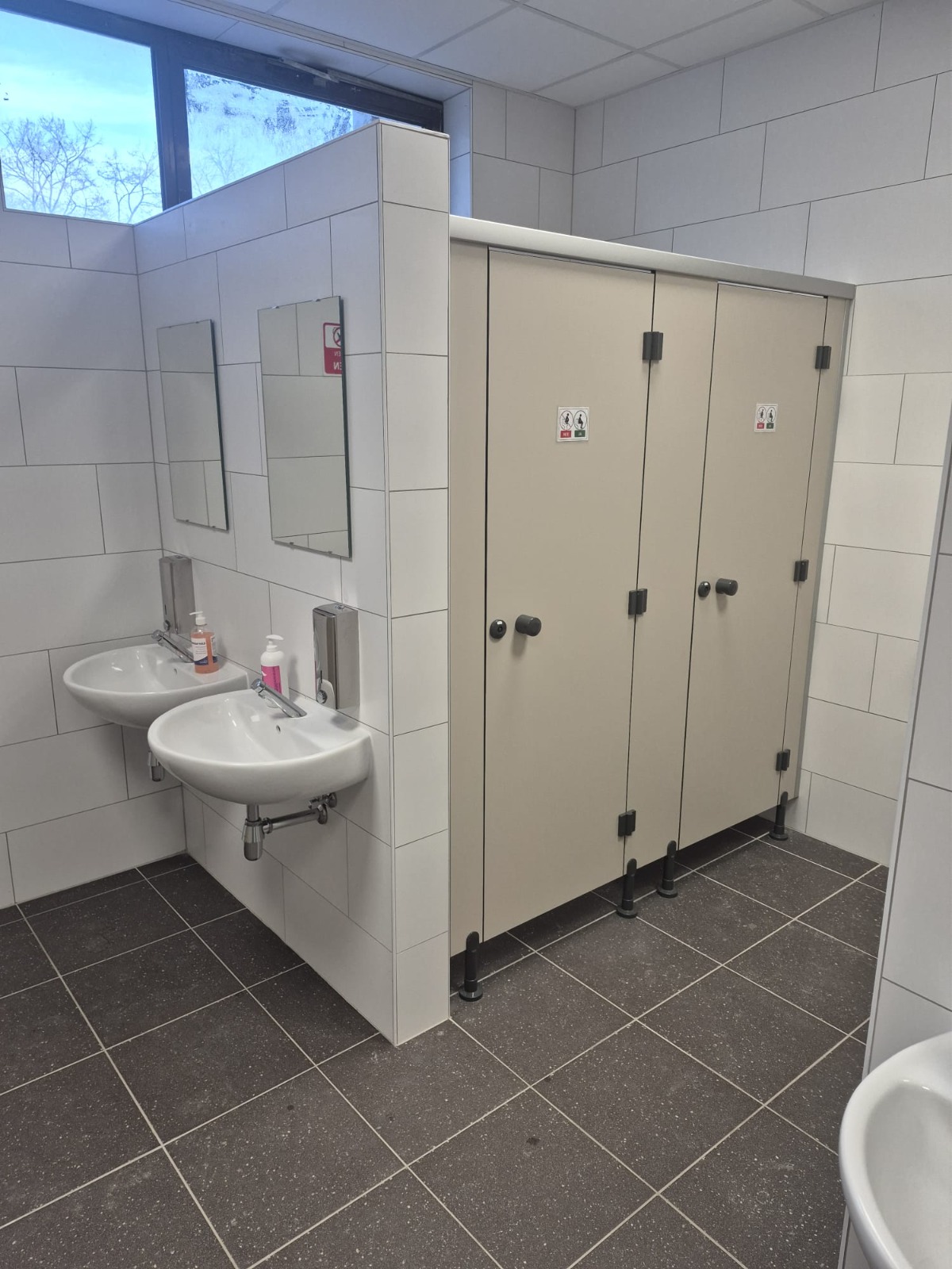 Afgewerkte sanitaire ruimte in een Brusselse school met betegelde scheidingswand, wastafels en toiletdeuren.