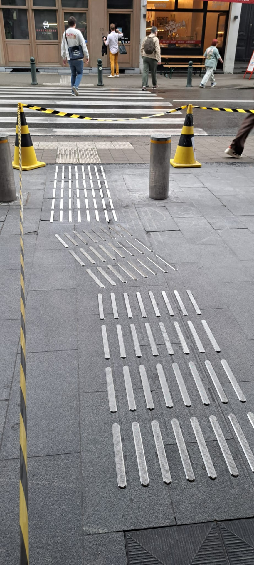 Metalen ribbels en noppen in een natuurstenen voetpad aan een oversteekplaats in Brussel.
