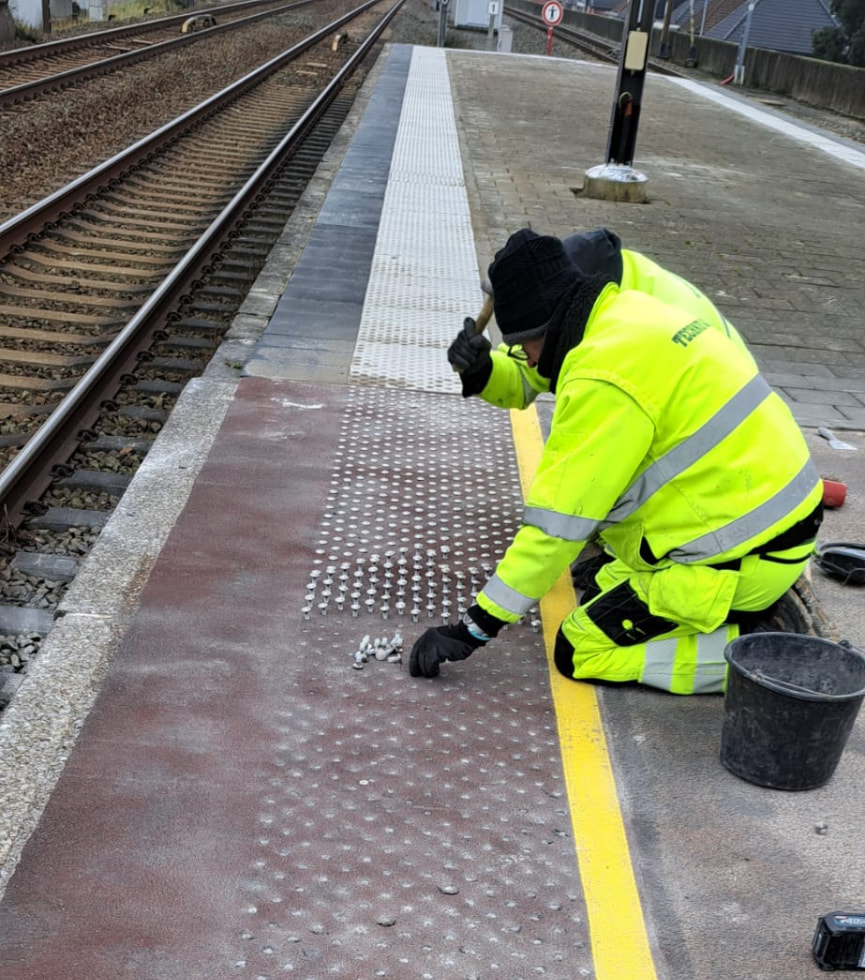 Plaatsing van metalen noppen op een treinperron in Landegem.