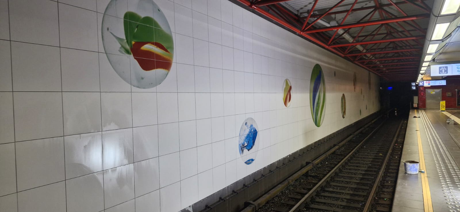 Afgewerkte betegelde tunnelwand met gekleurde ronde motieven langs het perron in Osseghem.